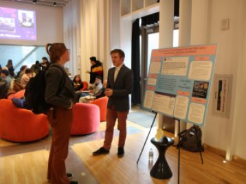 Ben Davis stands beside a large presentation board, explaining his project.